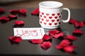 White cup with red hearts and an I-love-you-note on a black table, surrounded by red rose petals. Royalty Free Stock Photo