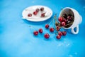 White cup with ripe berries of red sweet cherry and several berries in front of the cup. Composition on a blue Royalty Free Stock Photo