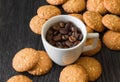 White cup with roasted coffee beans, biscuits with sesame seeds on a black background