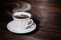 White cup and saucer with coffee and spoon on brown wooden surface, steam over the cup. Royalty Free Stock Photo