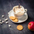 White cup on a saucer with hot cocoa. Morning breakfast. Dark wooden background.