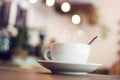 White cup with steaming hot coffee on table with bokeh background at coffee shop Royalty Free Stock Photo