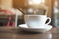 White cup with steaming hot coffee on table with bokeh background at cafe Royalty Free Stock Photo