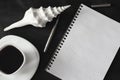 White cup of strong black coffee with metal pen, notepad and seashell on black surface close up. Royalty Free Stock Photo