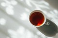 White cup of tea on abstract background of natural curtain shadow falling on white table