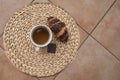 White cup of tea with a crispy croissant and a square of chocolate placed on a wicker mat Royalty Free Stock Photo