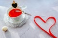 A white cup of tea on a delicate white saucer with a small black heart on a cup and with the original curved spoon on