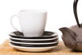 White cup of tea on different saucers with iron teapot on wooden