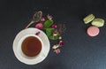 White cup of tea, rose buds and french macaroons on a black background Royalty Free Stock Photo