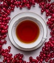 White cup of tea on a saucer on a white wooden background frame of red berries Viburnum close up top view