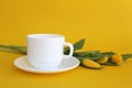 White cup of tea on a yellow background with yellow tulips