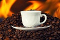 A white cup on top of a pile of roasted coffee beans with fire Royalty Free Stock Photo