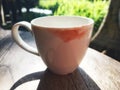 White cup on wooden table with sunshine reflection. Red lipstick color as lips dirty on edge after woman sip the tea. Royalty Free Stock Photo