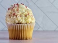 White cupcake with white frosting swirled high and curled white chocolate with red raspberry drizzle over the top, delicious sweet