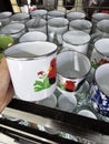 White cups displayed for sale, adorned with cartoon images of a black rooster with red wattles and green foliage