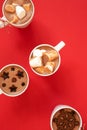 White cups with hot cocoa and marshmallows and spice cinnamon decor on red background, vertical. Winter holidays drinks