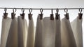 White curtain hangs on metal clothespins, in natural light from a window.