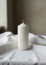 A white cylindrical candle is placed on a draped white fabric surface. The candle is unlit Royalty Free Stock Photo