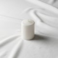 Cylindrical candle placed on a smooth white fabric surface casting a Royalty Free Stock Photo