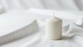 A white cylindrical candle is placed on a soft white fabric surface Royalty Free Stock Photo