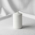 A white cylindrical candle with a small wick sits on a textured fabric surface Royalty Free Stock Photo