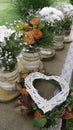 White daisy and orange roses in glass jars and wattle white heart in wreath Royalty Free Stock Photo