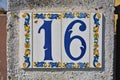 A white and decorated house number plaque, showing the number sixteen Royalty Free Stock Photo