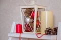 White decorative lantern with fir cones, silver and red bulbs inside. Candles and beads garland next to it. Merry Christmas