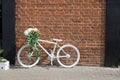 White decorative old bike with a basket of flowers against a brick wall. Copy space Royalty Free Stock Photo