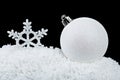 White decorative snowflake and christmas ball on white snow on black background