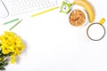 White desktop with keyboard, mouse, colorful stationery, yellow flowers, plate with granola, banana and large cup of milk