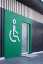 White disabled wheelchair sign with glass door on green wall and wooden panel wall decorations in public restroom Royalty Free Stock Photo