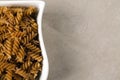 A white dish filled with uncooked wholewheat fusilli pasta