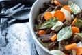 White dish with meat, carrots, onions and laurel on a black pan. Cooking appliances spoon and fork.