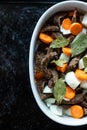 White dish with meat, carrots, onions and laurel on a black pan. Top view.