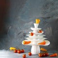 White dishes Pyramid of Christmas tree shape, yellow paprica on top, vegetables below on dark. Creative concept dishware, veg,