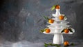 White dishes Pyramid like Christmas tree with mandarins with leaves on top, bunch below on dark Creative concept, dishware, veg, Royalty Free Stock Photo