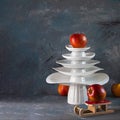 White dishes Pyramid like Christmas tree with red apples on top amd next to, on dark background. Creative concept, dishware, veg, Royalty Free Stock Photo