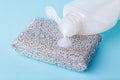 White dishwashing liquid flows from a plastic bottle onto a silver foam sponge. Purity and household chemicals. Kitchen detergent