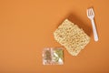 White disposable plastic fork, three block of dry instant noodles and spices on a brown background