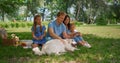 White dog lie down near family holding tablet on picnic. Father caress labrador.