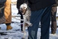 A white dog in a muzzle hides behind the feet of the owner among a crowd of people. The interaction of humans and animals