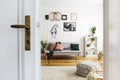 White door of bright living room interior with posters above grey sofa and pouf on carpet. Real photo Royalty Free Stock Photo