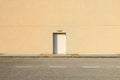 White door with a lamp above on yellow wall made of concrete mixed with small pebbles. Sidewalk and asphalt road in front. Royalty Free Stock Photo