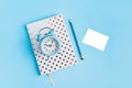 White dotted notebook, pecil, alarm clock and white piece of paper on blue background with copy space