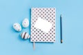 White dotted notebook, pecil, easter decorative eggs and white piece of paper on blue background