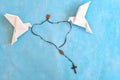 White dove origami carrying rosary or scapular in sky blue background.