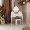 White dressing table with oval mirror and chair is part of cosy interior of beautiful bedroom