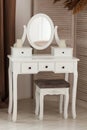 White dressing table with oval mirror and chair is part of cosy interior of beautiful contemporary bedroom