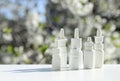 White dropper bottles, nose spray on background of spring flowering trees with copy space. Concept of allergy treatment. Nose